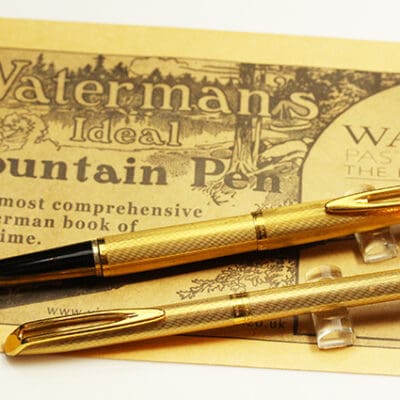 Two gold fountain pens on a piece of paper.